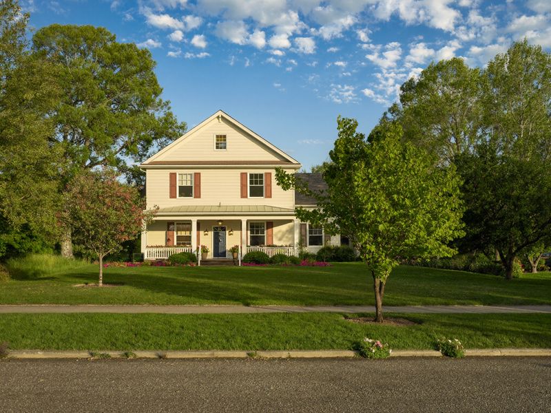 A sunny yellow farmhouse with a front porch and a green lawn